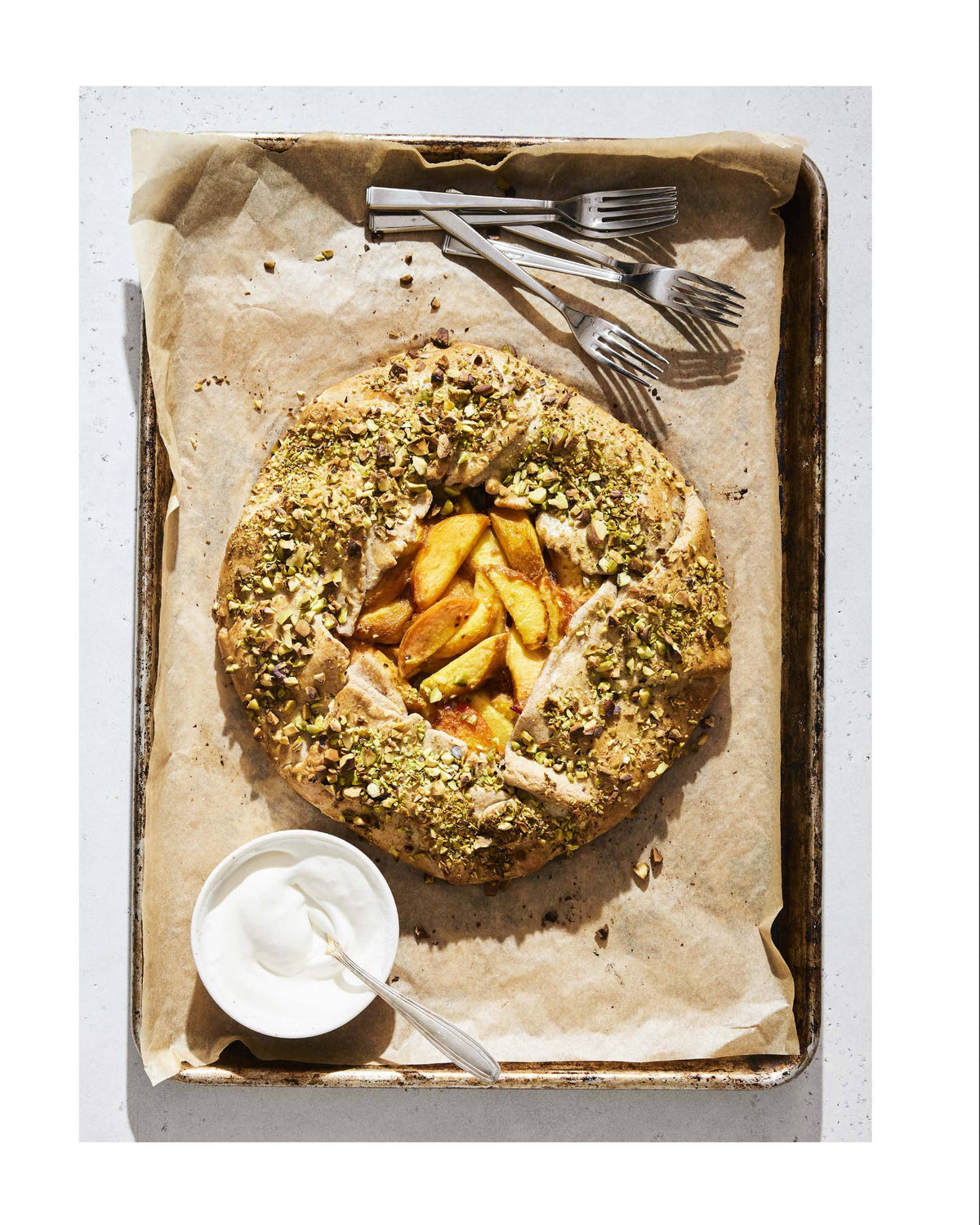 Pistachio-studded peach galette on a baking tray with utensils, recipe on the right.