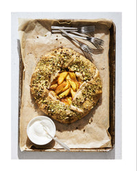 Pistachio-studded peach galette on a baking tray with utensils, recipe on the right.