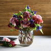 Bouquet of flowers in a clear pebbled vase on a wooden surface