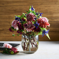 Bouquet of flowers in a clear pebbled vase on a wooden surface