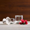 Two pebbled glass tumblers with silver coasters and red flowers on a wooden surface