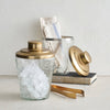 Decorative glass ice buckets with tongs and hammered gold lids on a light surface.