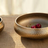 Hammered gold bowl on a textured surface with a blurred background