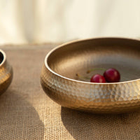 Hammered gold bowl on a textured surface with a blurred background